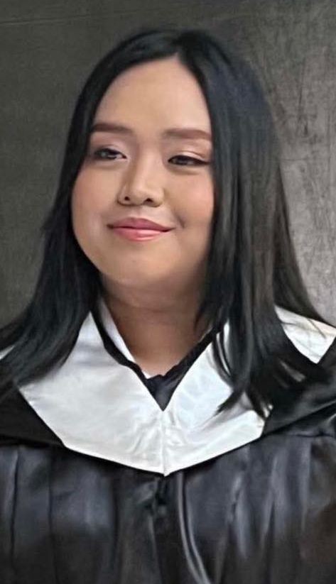 Person wearing a graduation gown and a white collar, standing in front of a dark background.