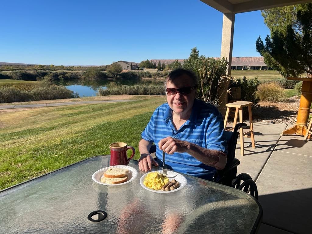 Person in sunglasses dining outdoors with scrambled eggs and toast on a patio overlooking a lush landscape.