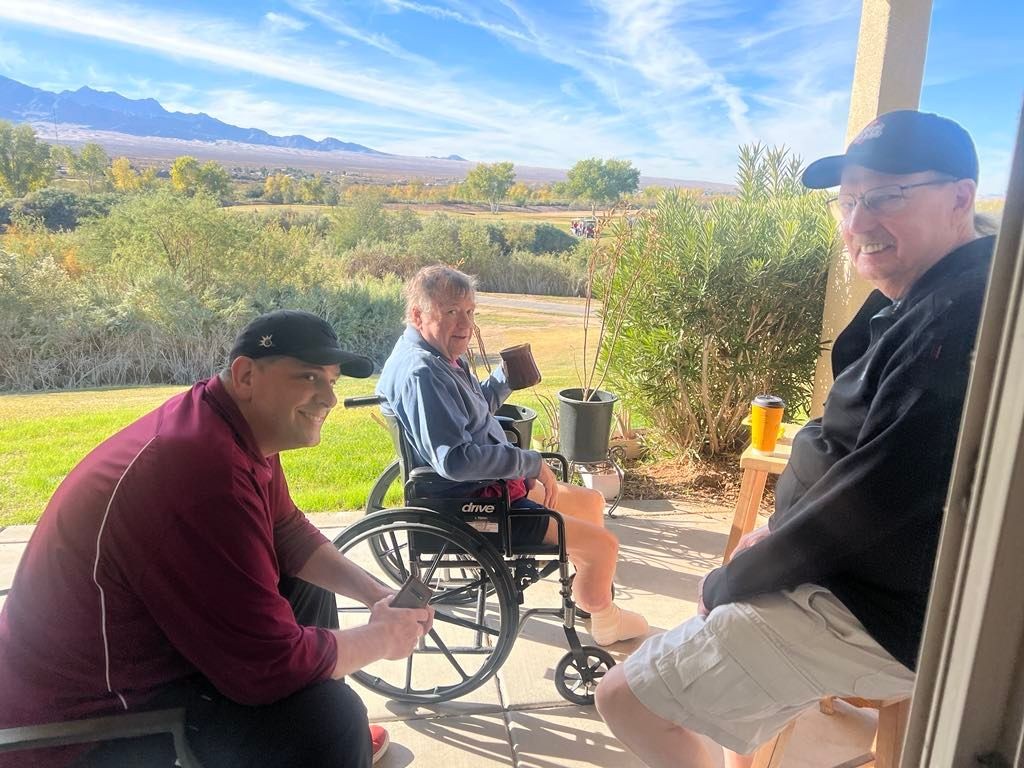 Three people sitting outside on a patio with a scenic view of mountains and greenery in the background.