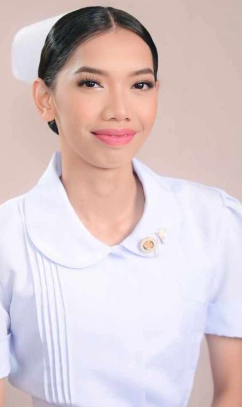 Person wearing a white uniform with a decorative pin and a cap, standing against a neutral background.