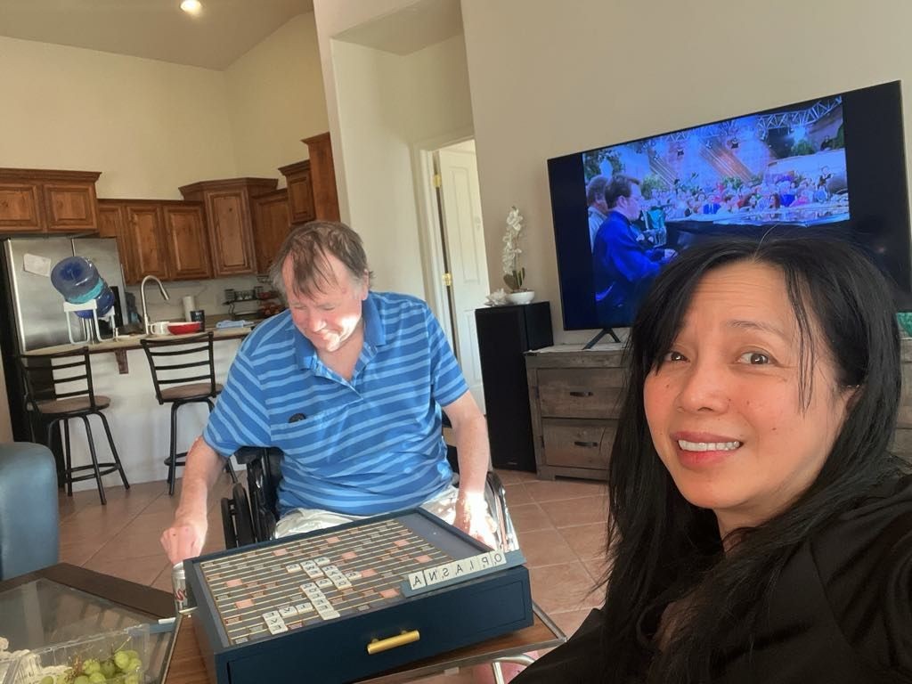 Man playing a board game in a living room while a woman smiles at the camera.